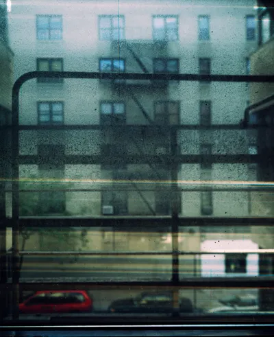Long-exposure scanning-back photograph of an apartment building facade seen through a grime-covered window, image 5 of 8 in the Grid Dirt Glass series.